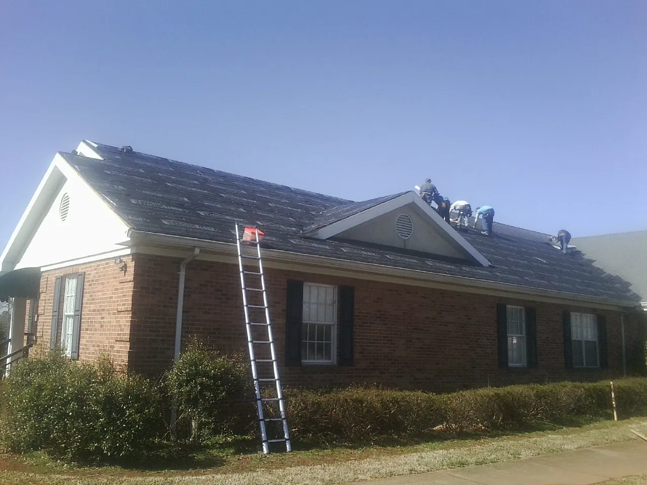 Crew tearing shingles off a brick ranch roof with a ladder set — Emergency Roof Repair work by our crew in Huntington