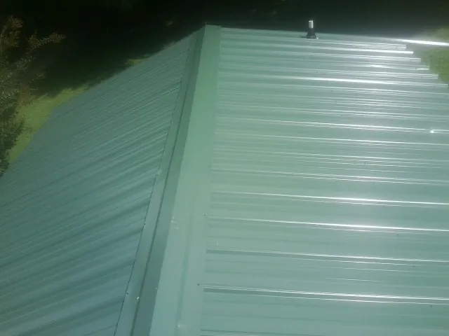 New green metal panels meeting at the ridge of a roof — Flat Roof Repair work by our crew in Huntington