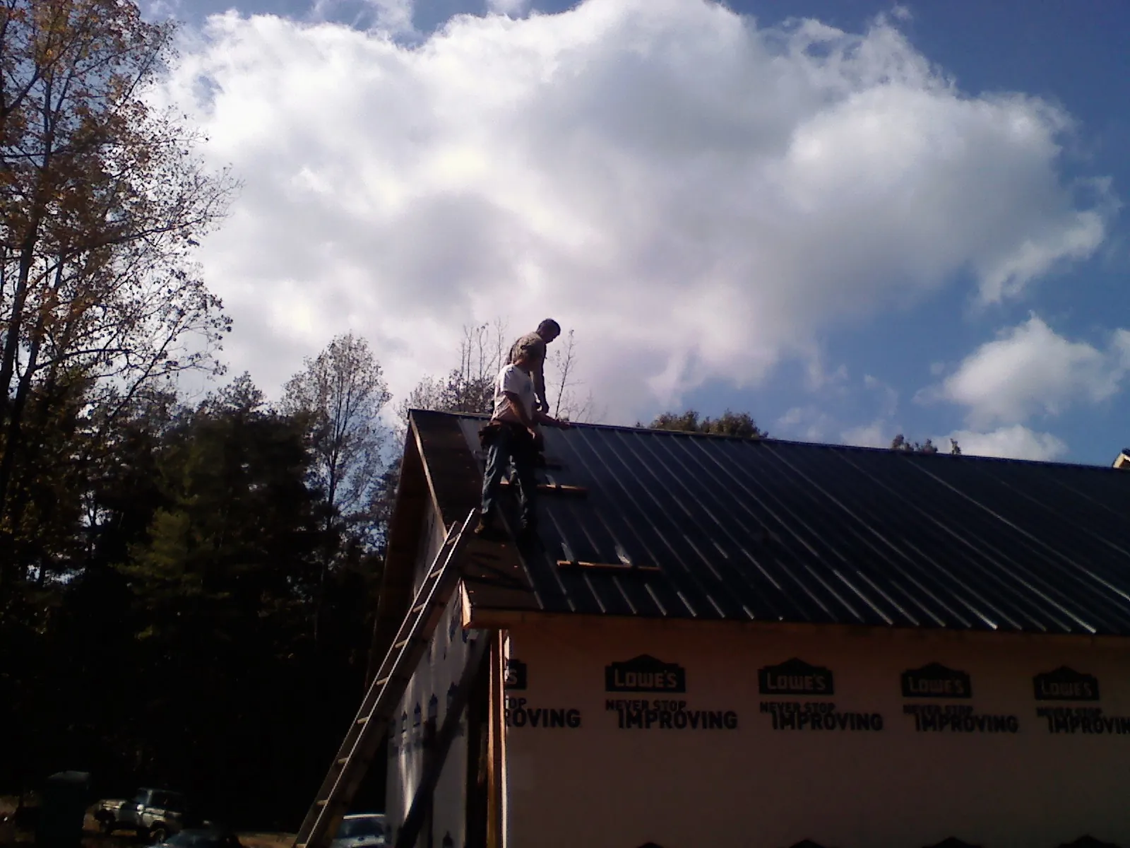 Roofer fastening dark metal panels high against a cloudy sky, from a Roof Inspection job in Huntington