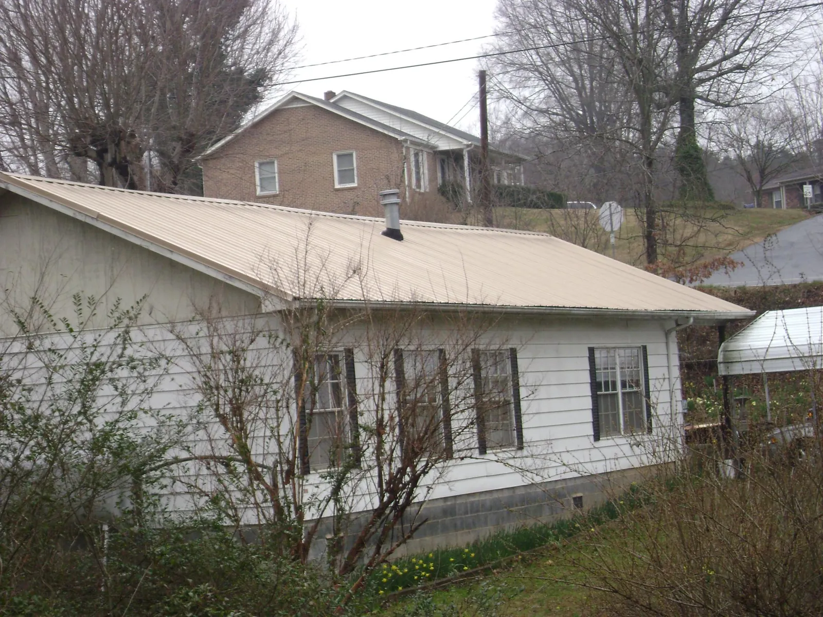 Tan metal roof on a white sided house set into a hillside — Commercial Roofing by Roofing Brothers in Huntington