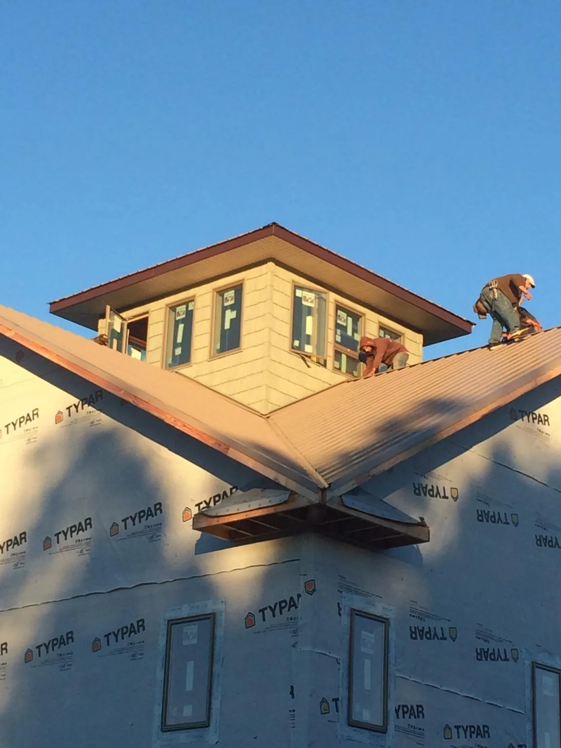 Roofers working around a rooftop cupola on a new metal roof at sunset — Roof Waterproofing in Huntington by Roofing Brothers